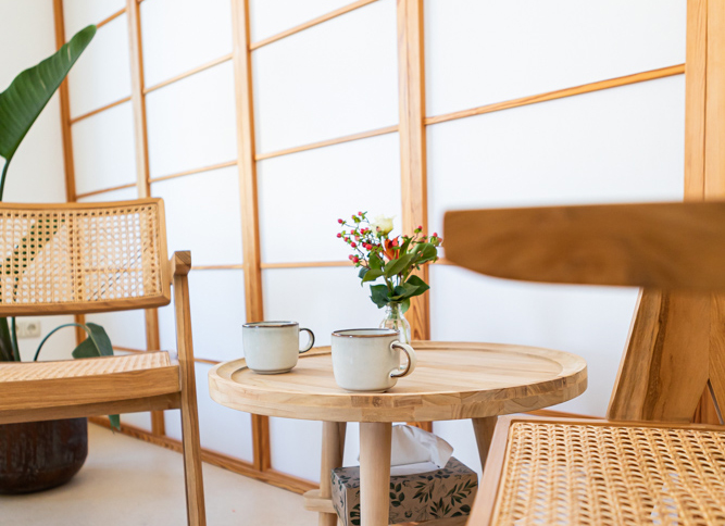 KARIN DANHOF - KARIN DANHOF - Hebamme, Psychotherapeutin (HP) & Yogalehrerin in Gießen Hintergrundbild der Startseite zeigt zwei Stühle an einem Kaffeetisch. Auf dem Tisch befinden sich zwei Tassen, eine Glasvase mit Blumen. Auf einer Ablage unter dem Tisch steht eine Taschentuch-Box.